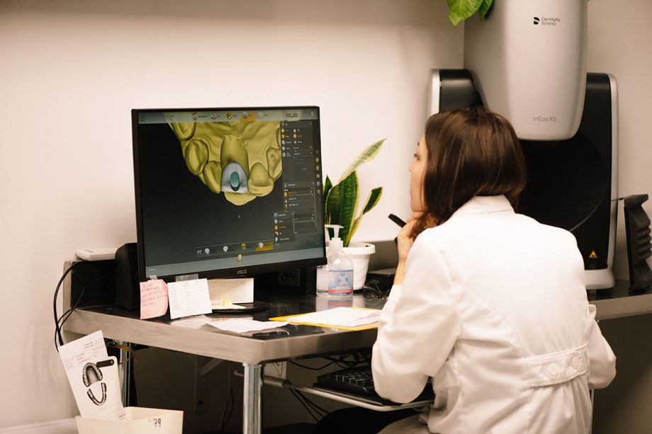 A lab technician SB Dental Laboratories sitting in front of a computer monitor with a 3D image of a dental implant